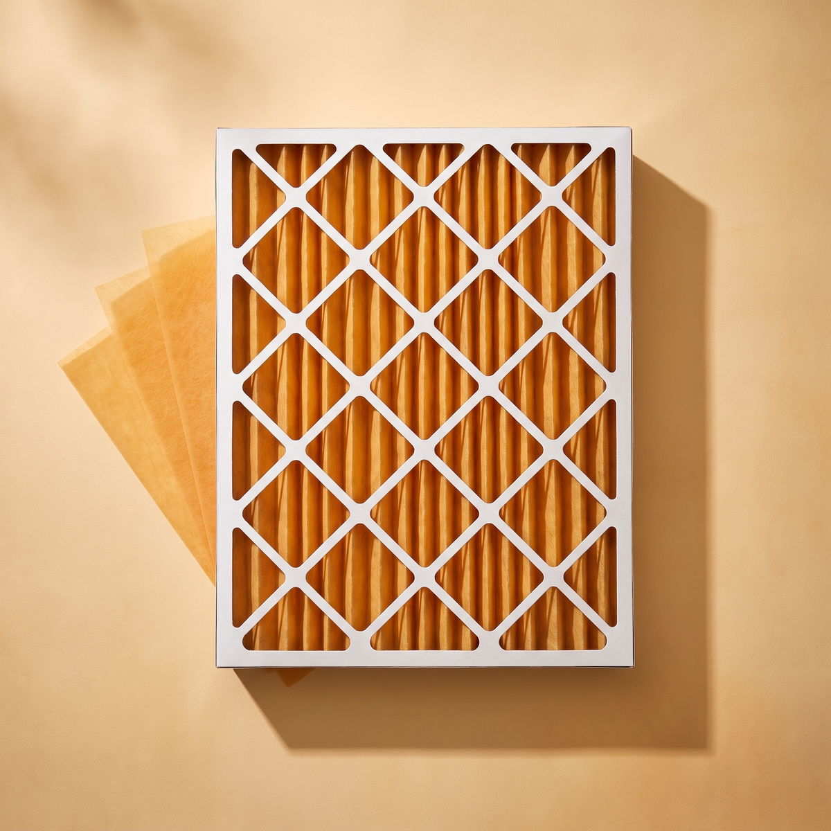 Two inch cardboard air filter frame with orange pleated screen media, flat lay on a warm tan backdrop