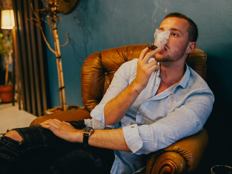 Man in a leather armchair exhaling cigar smoke in an indoor lounge